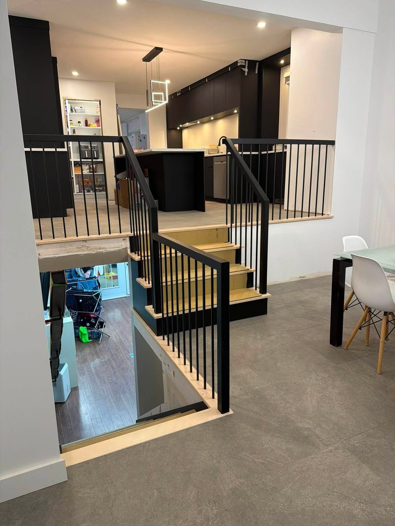 Escalier de bois clair avec garde-corps à barreaux noirs donnant sur une cuisine ouverte