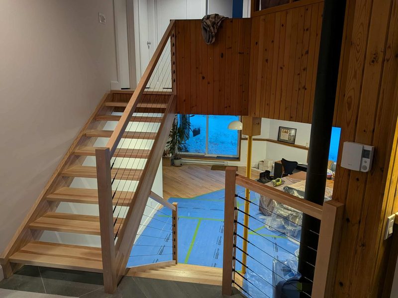 Escalier flottant en bois avec garde-corps à câbles, vu de l'étage d'un chalet