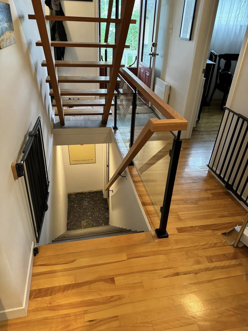 Escalier flottant en bois clair avec barreaux noirs, vu du palier