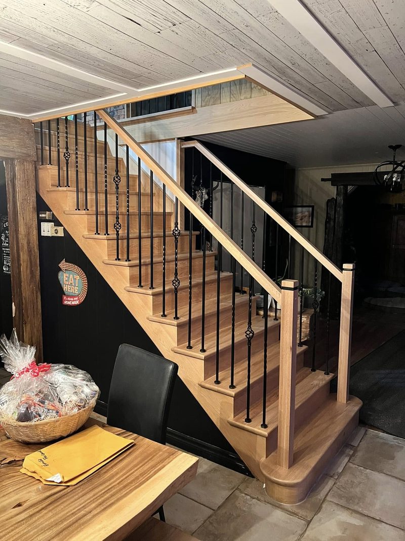 Escalier en bois naturel avec garde-corps à barreaux, ouvert sur la cuisine