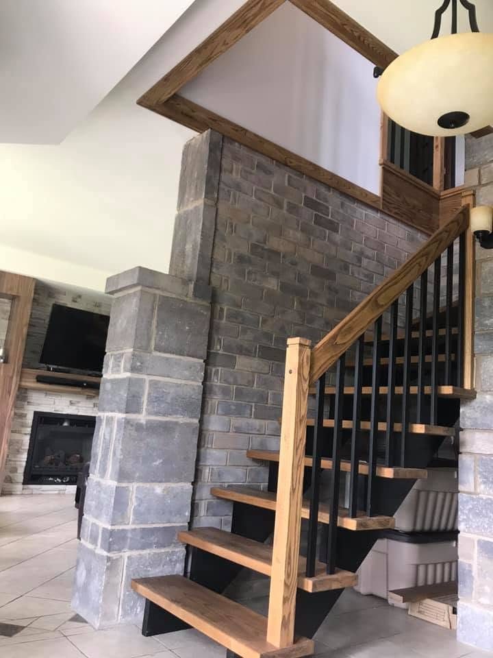 Escalier flottant en bois à limon noir devant une colonne de pierre